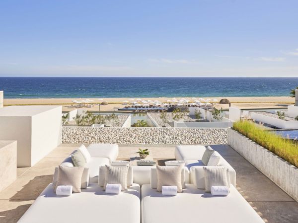 A luxurious patio with cushioned seating overlooks a beach and ocean, featuring elegant decor and a serene atmosphere.