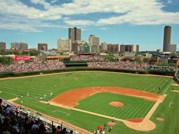 A baseball field with players, surrounded by a cityscape and a crowd in the stands under a partly cloudy sky.