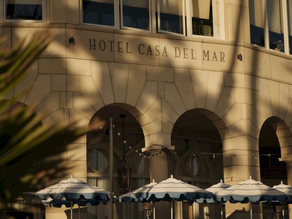 The image shows the facade of Hotel Casa Del Mar, with arched windows and striped umbrellas outside, creating a classic seaside ambiance.