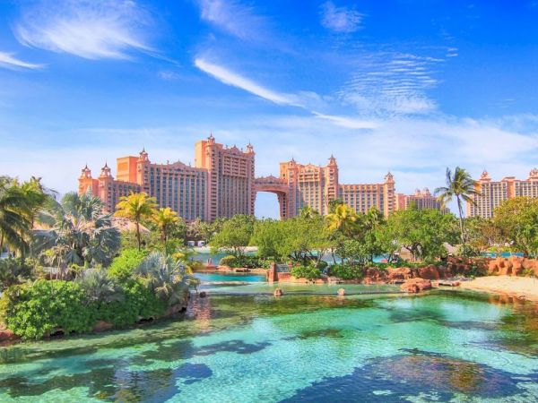 A large, luxurious resort with tall, ornate buildings surrounded by lush greenery and a clear turquoise lagoon under a bright blue sky.