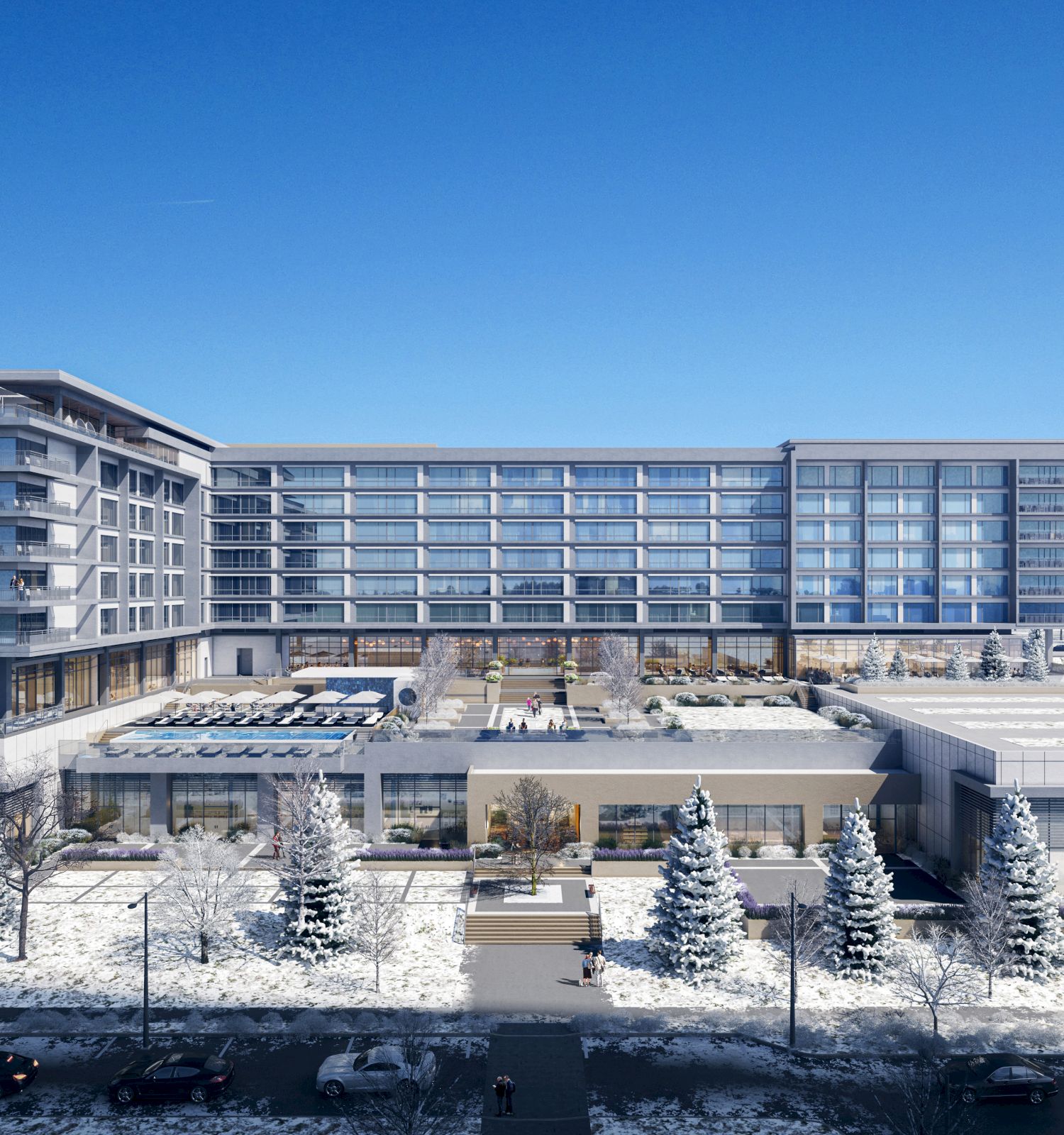 A modern multi-story building with large windows and balconies is surrounded by snow-covered trees and paths, set against a clear blue sky.