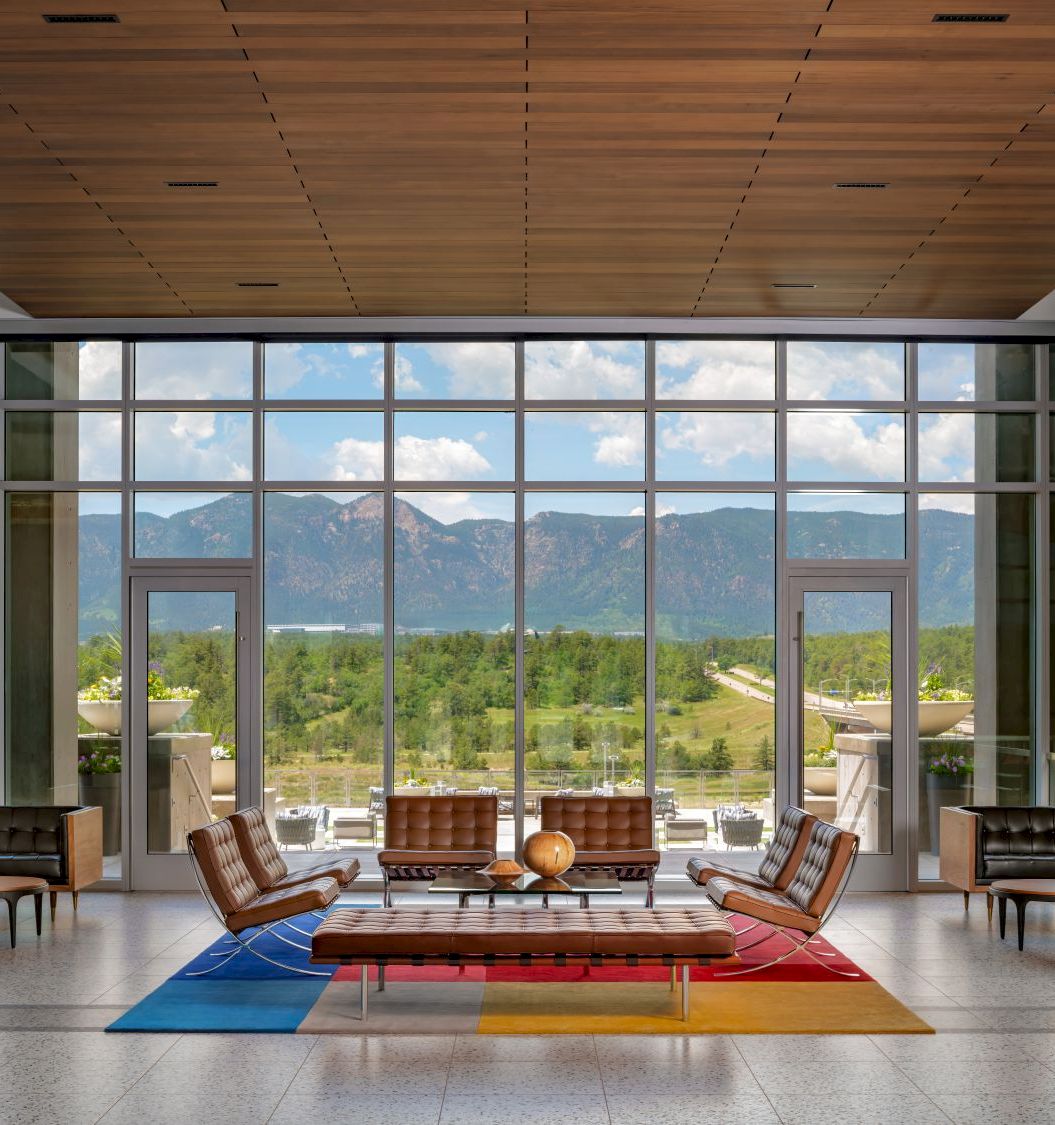 A modern lounge with leather chairs, rugs, and a wall of windows overlooking green mountains and a valley,